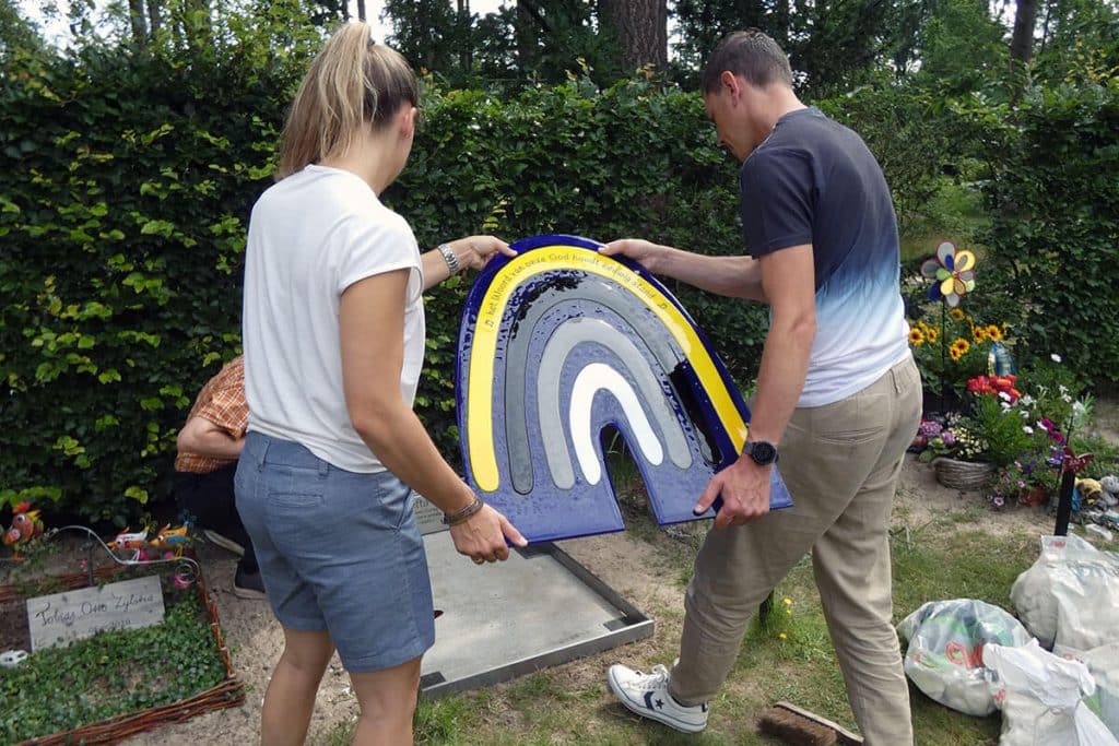 ouders dragen samen glazen grafsteen met regenboog
